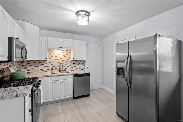 kitchen with sink, tasteful backsplash, appliances with stainless steel finishes, light stone countertops, and white cabinets