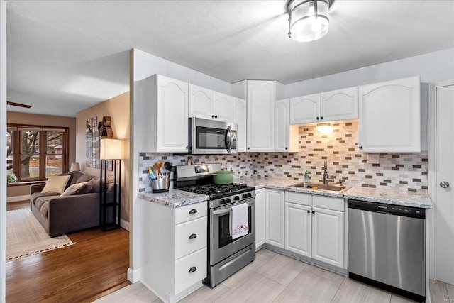 kitchen featuring stainless steel appliances, sink, white cabinets, and light stone counters