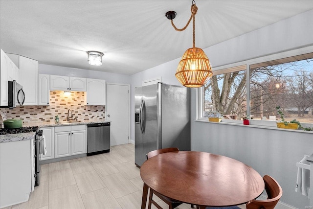 kitchen featuring sink, white cabinetry, hanging light fixtures, stainless steel appliances, and decorative backsplash