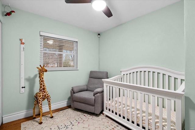 bedroom with light hardwood / wood-style flooring, a nursery area, and ceiling fan