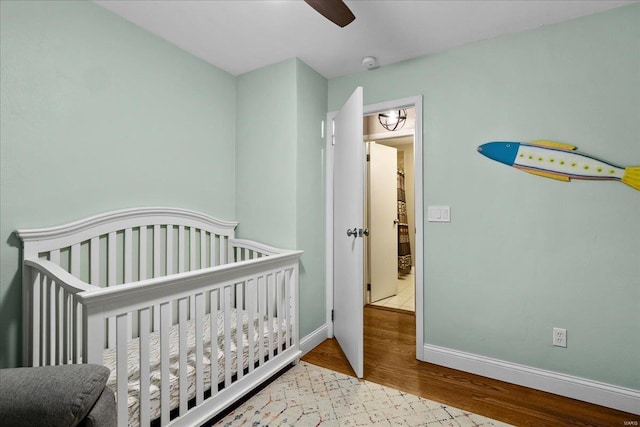 bedroom with a crib, ceiling fan, and light hardwood / wood-style flooring