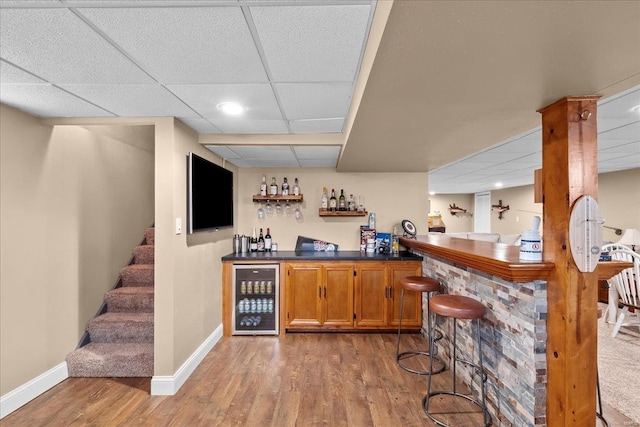 bar with wine cooler, a paneled ceiling, and light hardwood / wood-style floors