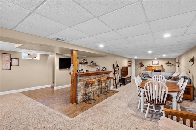 dining room with a drop ceiling, hardwood / wood-style flooring, and bar area