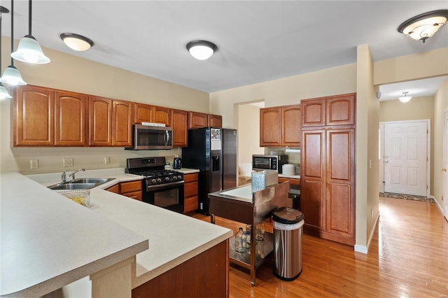 kitchen with decorative light fixtures, sink, light wood-type flooring, and black appliances