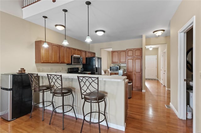 kitchen featuring pendant lighting, a breakfast bar area, light hardwood / wood-style floors, kitchen peninsula, and stainless steel appliances