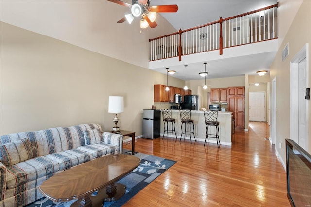 living room featuring a towering ceiling, ceiling fan, and light wood-type flooring