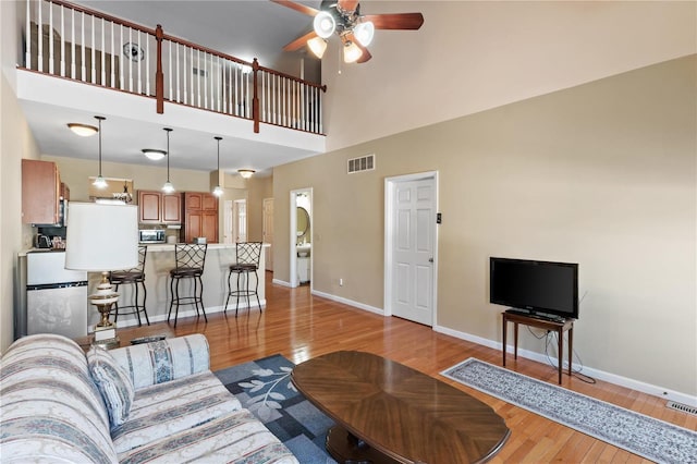 living room featuring a towering ceiling, ceiling fan, and light hardwood / wood-style flooring