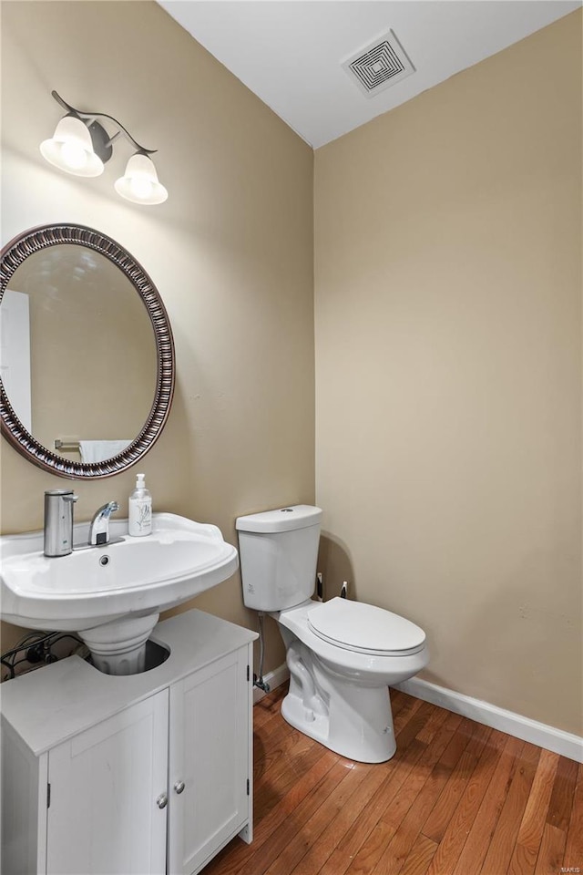 bathroom featuring wood-type flooring, visible vents, toilet, a sink, and baseboards