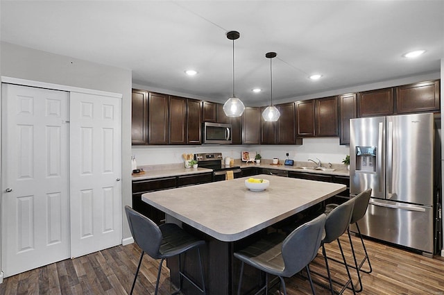 kitchen with appliances with stainless steel finishes, dark hardwood / wood-style floors, a center island, a kitchen bar, and decorative light fixtures