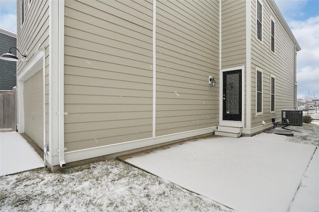 snow covered property with a garage, a patio, and central AC unit