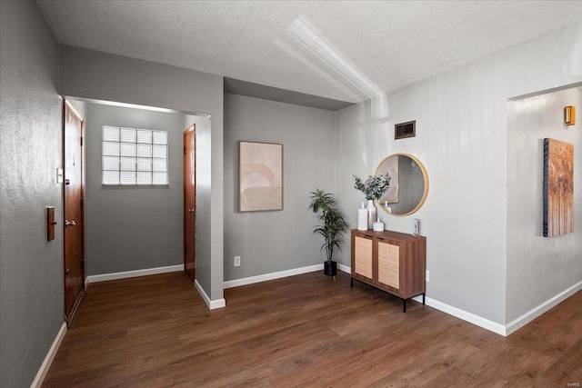 hall with a textured ceiling, wood finished floors, visible vents, and baseboards