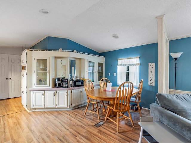 dining space with ornamental molding, vaulted ceiling, light hardwood / wood-style floors, and a textured ceiling