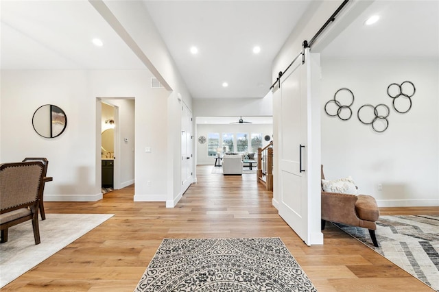 hall featuring light wood-type flooring, baseboards, visible vents, and a barn door