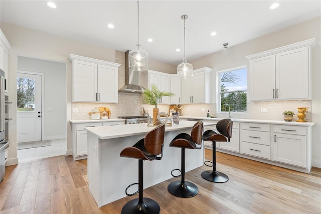 kitchen featuring a kitchen breakfast bar, wall chimney range hood, white cabinetry, light countertops, and light wood finished floors