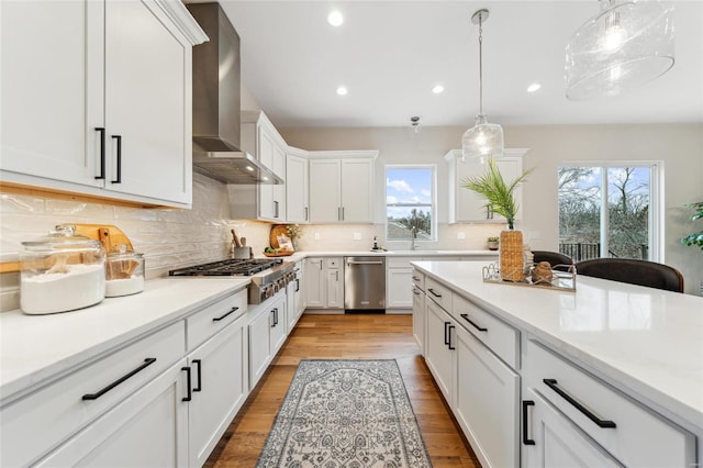 kitchen with wall chimney range hood, white cabinets, appliances with stainless steel finishes, and a healthy amount of sunlight