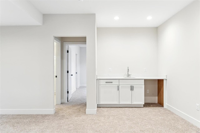 bar featuring wet bar, light colored carpet, a sink, and baseboards