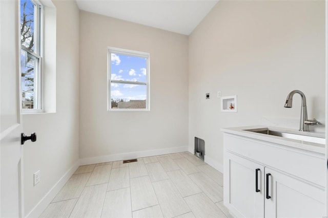 clothes washing area with baseboards, hookup for an electric dryer, a sink, and cabinet space