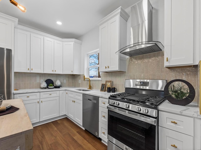 kitchen with appliances with stainless steel finishes, sink, wall chimney range hood, and white cabinets