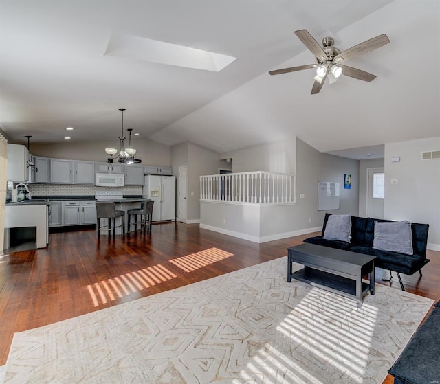 living room featuring ceiling fan with notable chandelier, dark hardwood / wood-style flooring, and vaulted ceiling