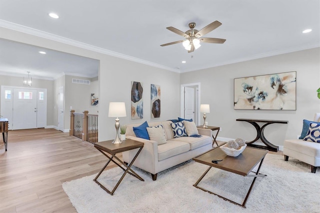 living room with ceiling fan with notable chandelier, ornamental molding, and light hardwood / wood-style floors