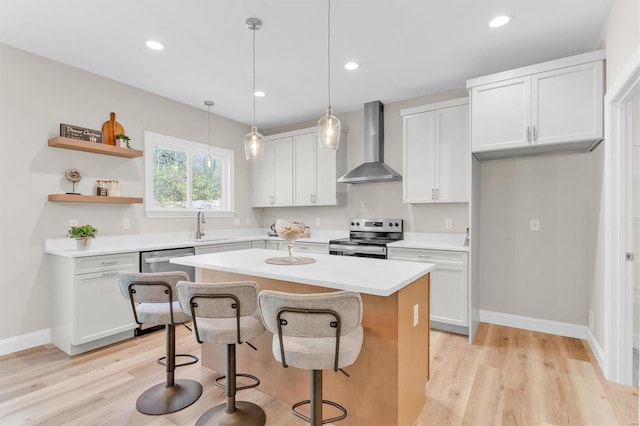 kitchen with appliances with stainless steel finishes, a center island, wall chimney range hood, and white cabinets