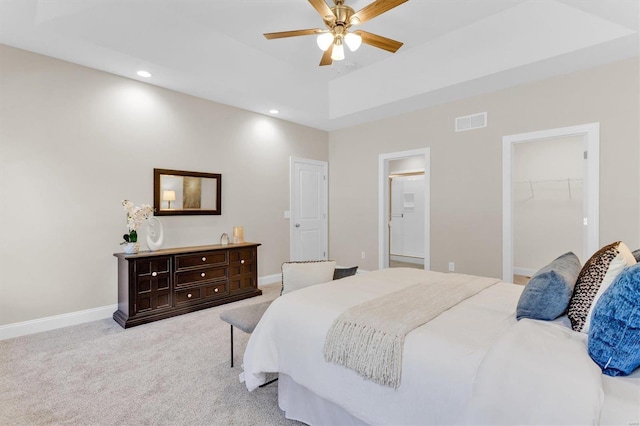 bedroom with ensuite bath, a spacious closet, light carpet, a tray ceiling, and ceiling fan