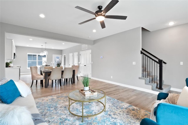 living room featuring ceiling fan with notable chandelier and light hardwood / wood-style floors