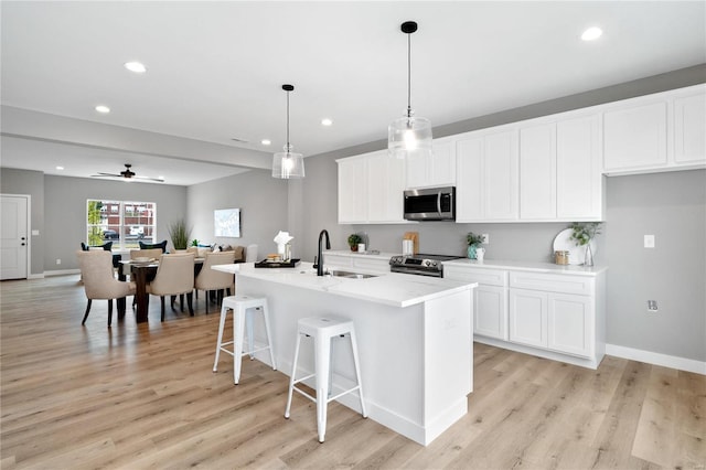 kitchen with white cabinetry, stainless steel appliances, sink, and an island with sink