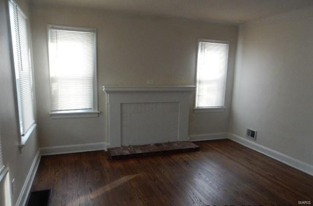 unfurnished living room with visible vents, a fireplace with raised hearth, baseboards, and wood finished floors