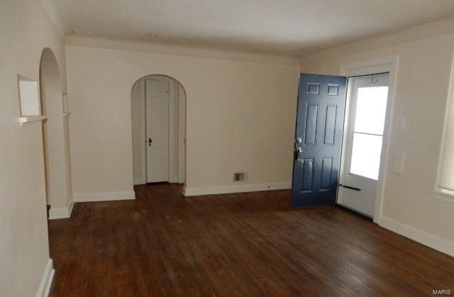 unfurnished room with wood finished floors, arched walkways, and baseboards