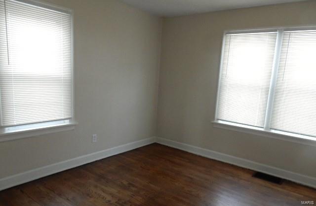 unfurnished room featuring visible vents, baseboards, a healthy amount of sunlight, and dark wood finished floors