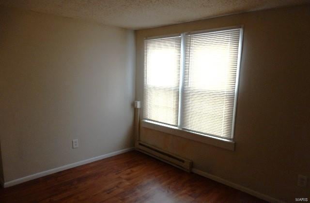 spare room featuring a textured ceiling, wood finished floors, baseboards, and a baseboard radiator