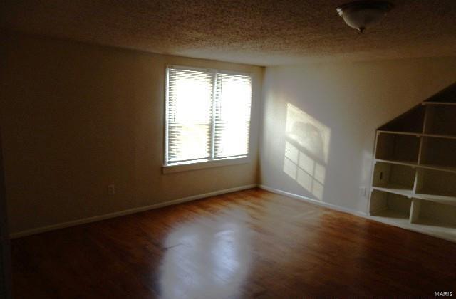 empty room featuring wood finished floors, baseboards, and a textured ceiling