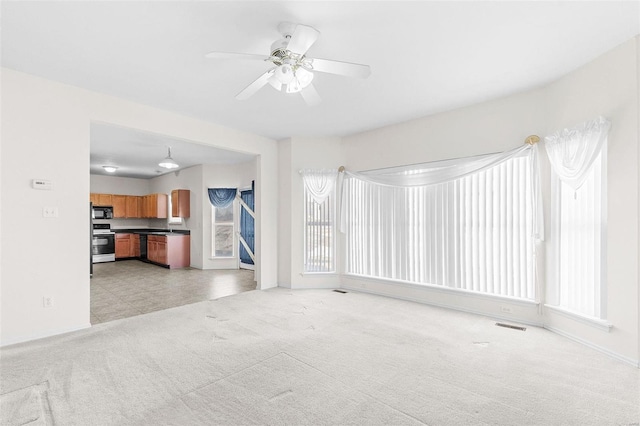 unfurnished living room featuring a healthy amount of sunlight, light carpet, and ceiling fan