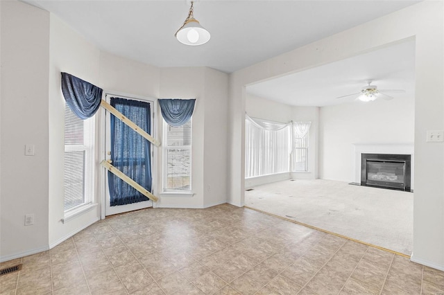 unfurnished living room with plenty of natural light, ceiling fan, and carpet