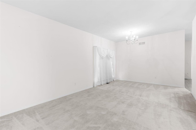 spare room featuring light carpet and a notable chandelier