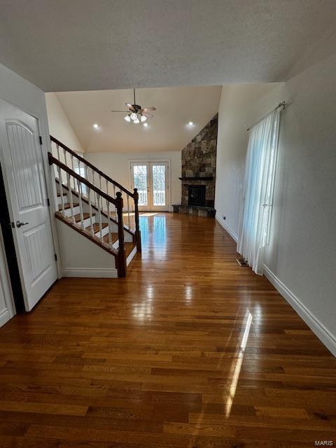 unfurnished living room with vaulted ceiling, dark hardwood / wood-style floors, a fireplace, ceiling fan, and french doors