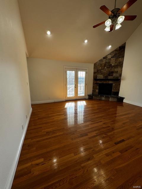 unfurnished living room with dark wood-type flooring, french doors, vaulted ceiling, ceiling fan, and a fireplace