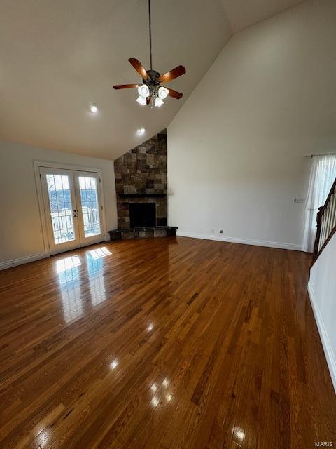 unfurnished living room featuring a stone fireplace, dark hardwood / wood-style floors, high vaulted ceiling, ceiling fan, and french doors