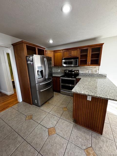 kitchen with light stone counters, a textured ceiling, appliances with stainless steel finishes, kitchen peninsula, and backsplash