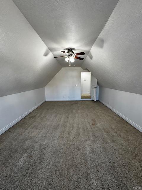 bonus room featuring vaulted ceiling, ceiling fan, dark carpet, and a textured ceiling