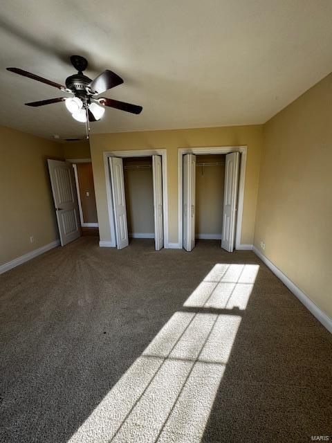 unfurnished bedroom featuring dark colored carpet, ceiling fan, and two closets