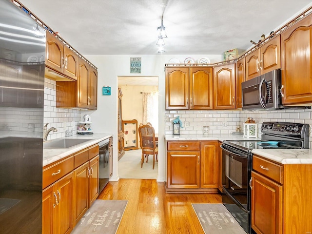 kitchen with appliances with stainless steel finishes, sink, light hardwood / wood-style floors, and decorative backsplash