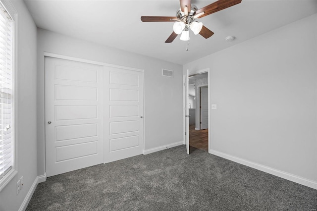 unfurnished bedroom featuring baseboards, visible vents, a ceiling fan, dark carpet, and a closet