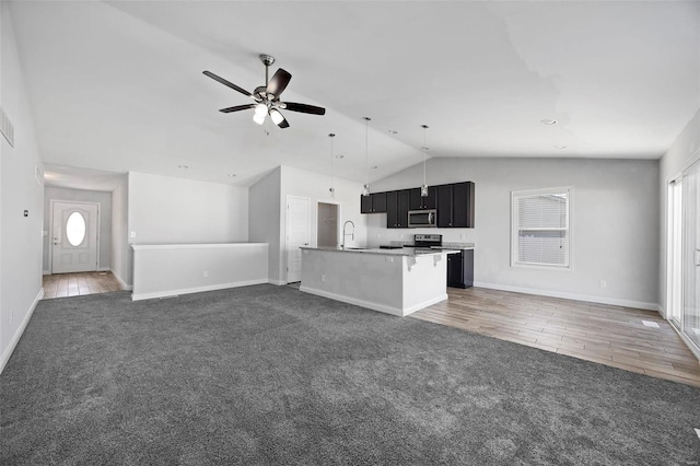 kitchen featuring carpet floors, stainless steel microwave, open floor plan, and dark cabinetry