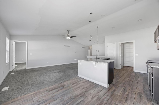 kitchen with a ceiling fan, an island with sink, dark wood-style flooring, vaulted ceiling, and a sink