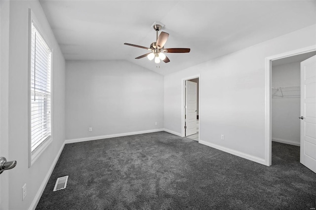 unfurnished bedroom featuring carpet floors, visible vents, baseboards, vaulted ceiling, and a walk in closet