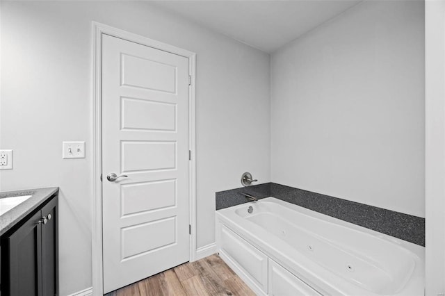 bathroom with a jetted tub, wood finished floors, and vanity