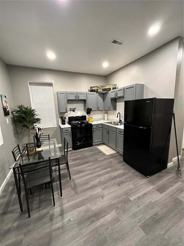 kitchen featuring sink, gray cabinetry, decorative backsplash, black appliances, and light hardwood / wood-style flooring