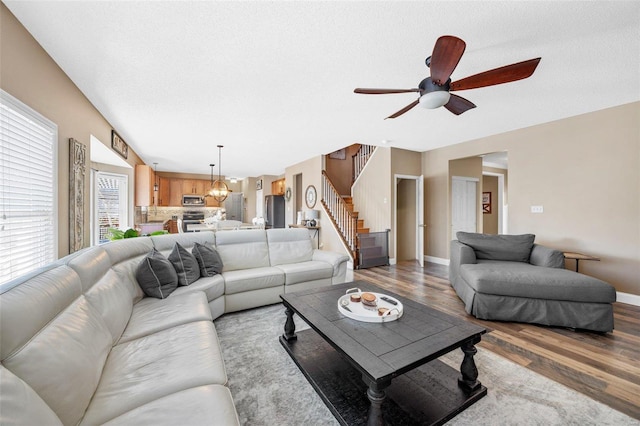 living room featuring ceiling fan with notable chandelier, hardwood / wood-style floors, and a textured ceiling